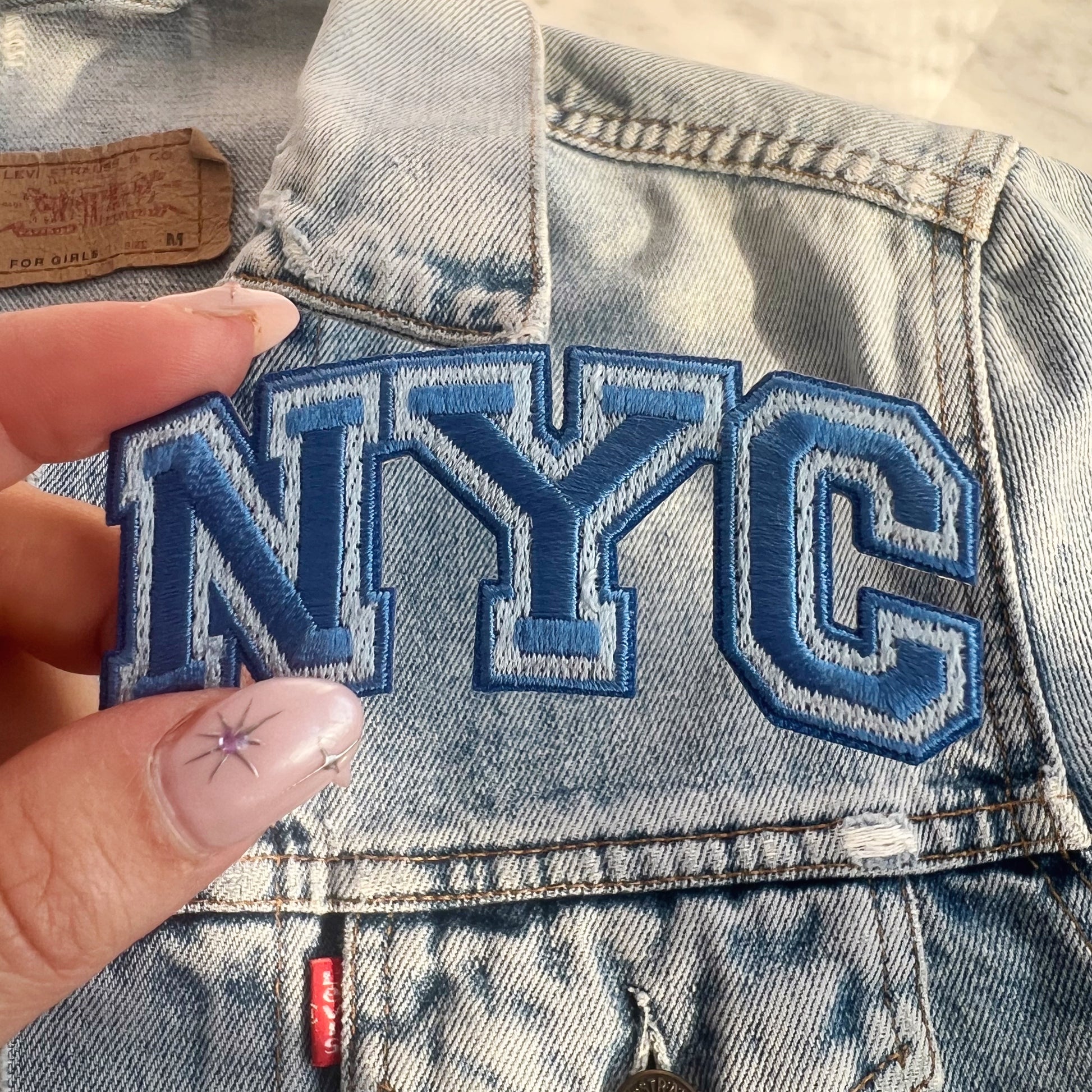 NYC Patch -Embroidered Iron On Patches for Jackets - New York City Souvenir - Wildflower + Co blue on jacket hand